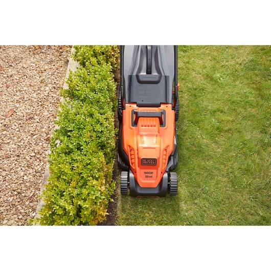 Top view of BLACKDECKER BEMW471ES lawn mower cutting grass along garden edge, orange housing, 1600W, 38cm width.