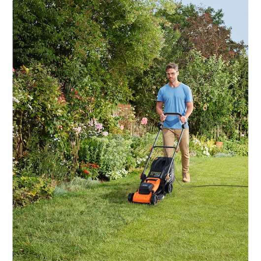 BLACKDECKER BEMWP340-QS lawn mower with orange and black design mowing grass in a garden outdoors.