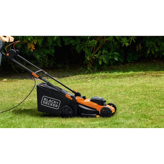 BLACK+DECKER BEMWP340-QS orange and black electric lawn mower on grass, side view.