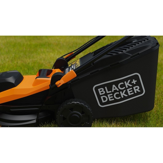 Photo of BLACK+DECKER BEMWP340-QS electric lawn mower side view on grass, showing black and orange body and rear grass collection bag.
