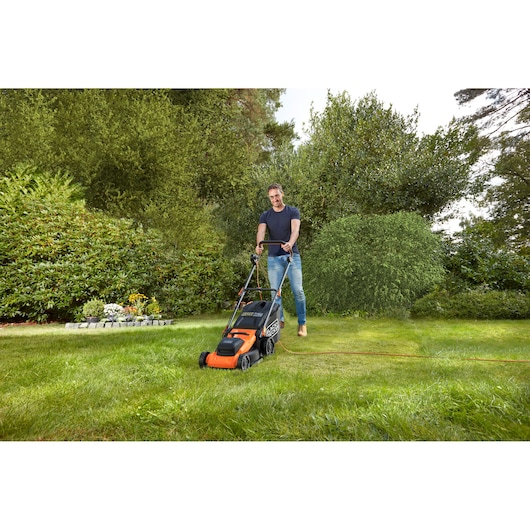 Photo of BLACK+DECKER BEMWP400-QS electric lawn mower in use on a green lawn with garden plants in the background.