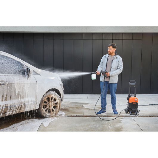 BLACKDECKER BEPW2000 pressure washer spraying foam on a dirty car outdoors.