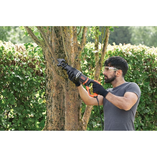 Person using BLACKDECKER BES301K reciprocating saw to cut tree branch in outdoor garden.