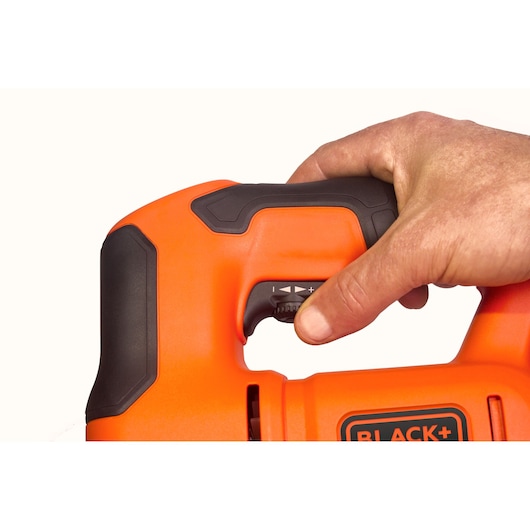 Close-up photo of a hand adjusting the trigger on BLACK+DECKER jigsaw BES603, orange and black handle, white background.