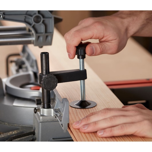 Close-up of hand using BLACK+DECKER BES700 miter saw clamp to secure wooden board during cutting.