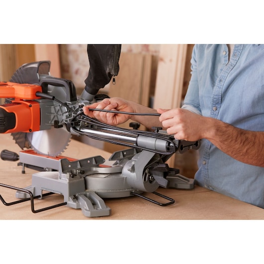 Photo of BLACKDECKER BES700 sliding miter saw on workbench with person adjusting cord, close-up view.