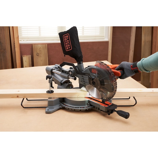 BLACKDECKER BES701 miter saw cutting wood on tabletop, side angle, dust bag visible.