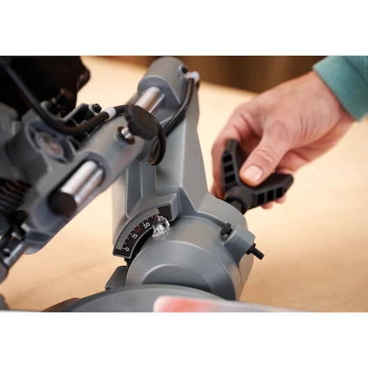 BLACK+DECKER BES701 miter saw close-up showing angle adjustment knob and scale being set by hand.