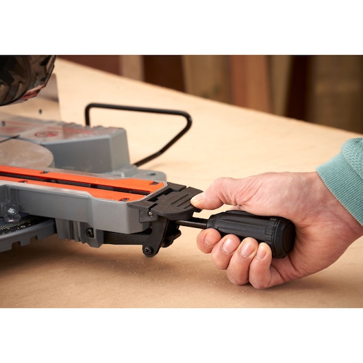 Close-up photo of hand adjusting BLACK+DECKER BES701 miter saw with black handle on wooden workbench.