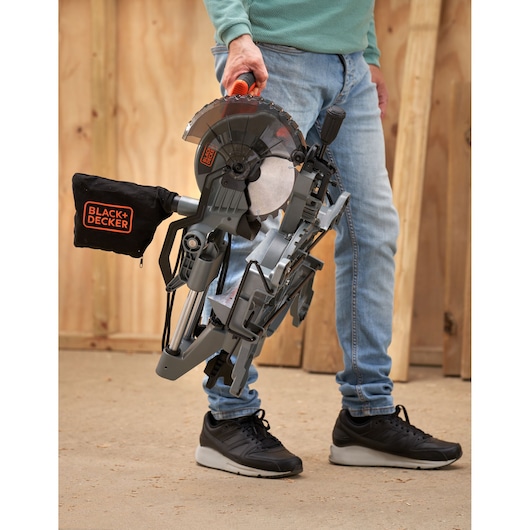 Photo of a person holding a BLACK+DECKER BES701 miter saw by the handle, standing on a workshop floor.