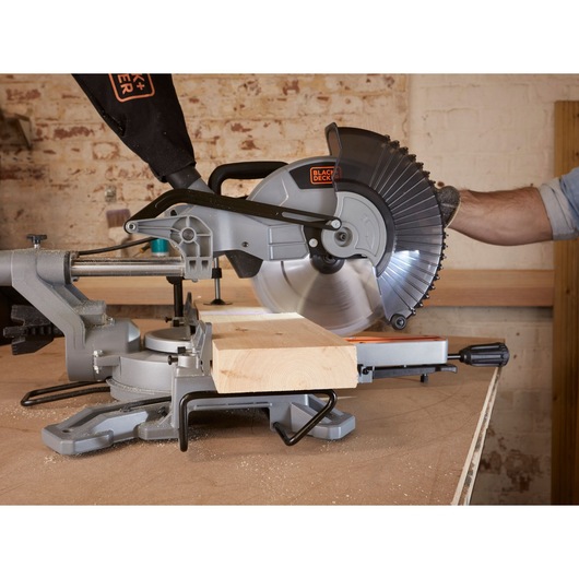 BLACKDECKER BES710 miter saw side view cutting wood plank on workbench.
