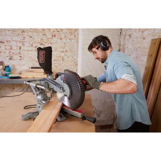 Photo of BLACK+DECKER BES710 miter saw in use, cutting wood on a workbench in a workshop setting.
