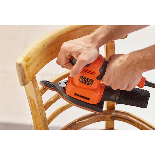 Photo of BLACK+DECKER BEW200K sander being used on a wooden chair, close-up view.