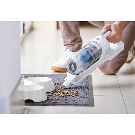 BLACKDECKER BHFEA420J handheld vacuum cleaner cleaning pet food from mat near bowls.