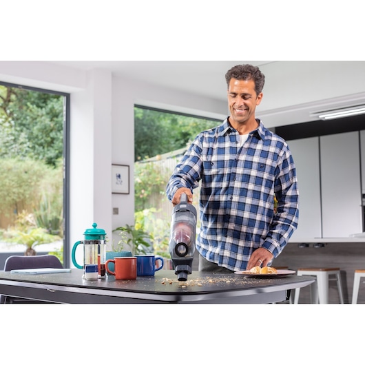 BLACKDECKER BHFEA520J handheld vacuum cleaning crumbs on a kitchen table next to mugs and a French press.