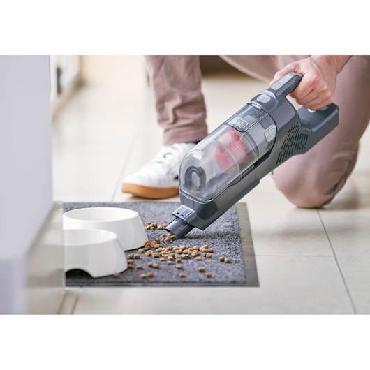 BLACKDECKER BHFEA520J handheld vacuum cleaning pet food near white bowls on gray mat.
