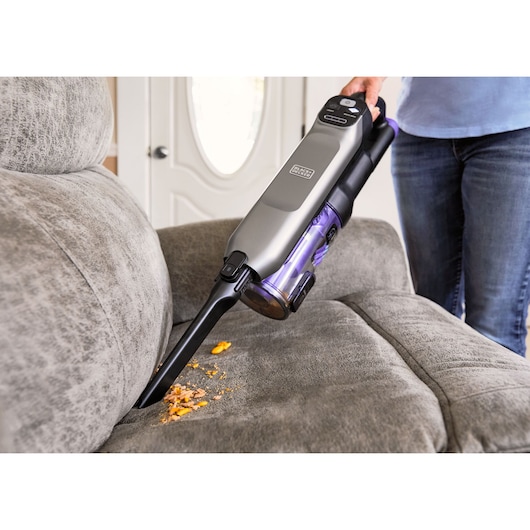 BLACKDECKER BHFEA640WP handheld vacuum cleaning crumbs on gray sofa, angled side view.