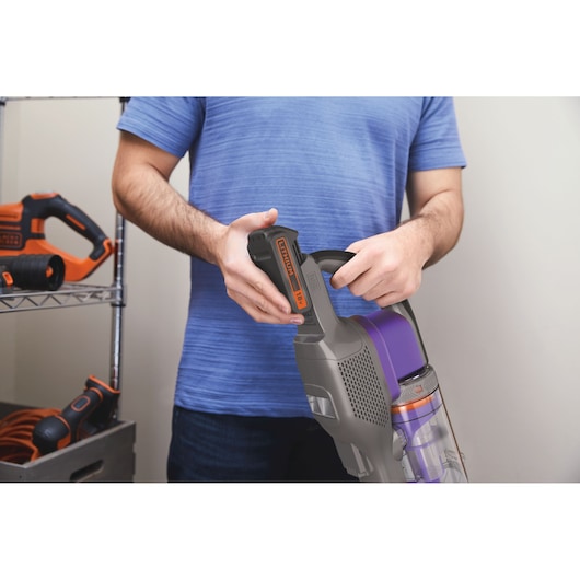 Photo of person holding BLACK+DECKER BHFEV182CP cordless vacuum with visible removable 18V battery.