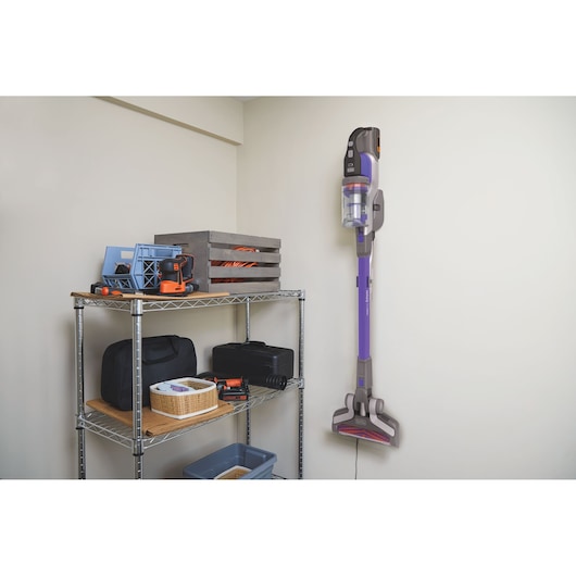 BLACKDECKER BHFEV362DP cordless stick vacuum mounted on wall in utility room beside metal shelving with tools.