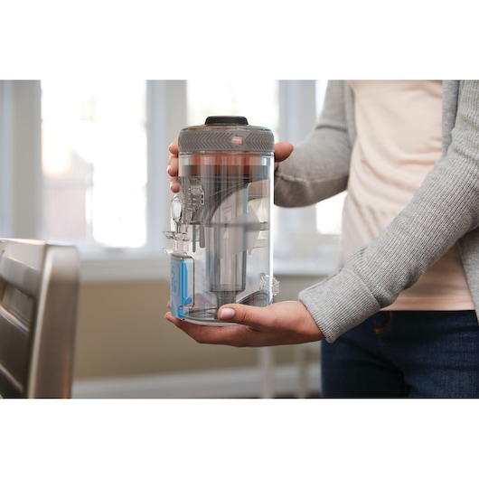Photo of a person holding a BLACKDECKER BHFEV362D vacuum dust canister in a home setting.