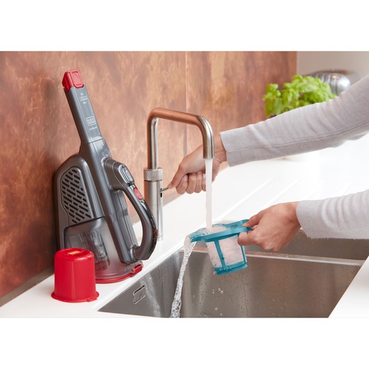Photo of BLACK+DECKER BHHV315B handheld vacuum with its filter being rinsed under a kitchen faucet.