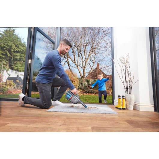 BLACKDECKER BHHV520BF handheld vacuum cleaner used on rug indoors near open glass door.