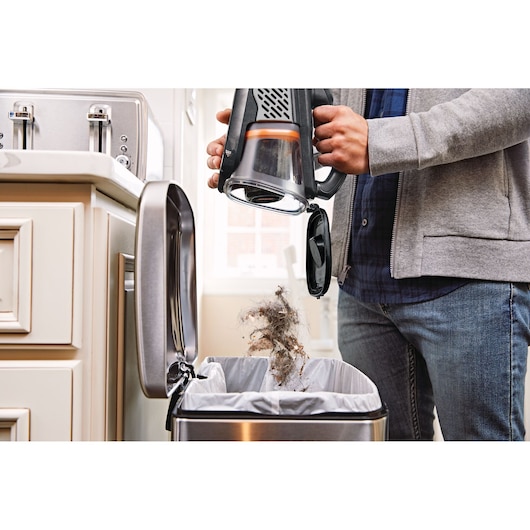 BLACKDECKER BHHV520JF handheld vacuum being emptied into a kitchen trash bin.