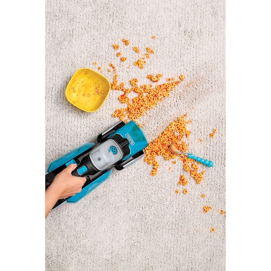 BLACK+DECKER BHSB320JP vacuum cleaner on beige carpet cleaning scattered orange cereal near a yellow bowl and blue spoon.