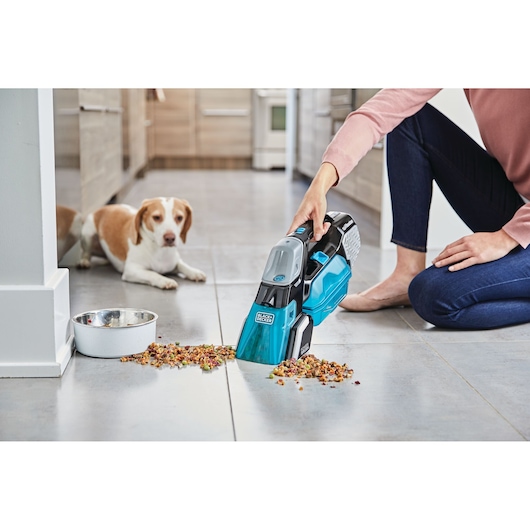 BLACK+DECKER BHSB320JP handheld vacuum cleaning spilled pet food on kitchen floor near a dog.
