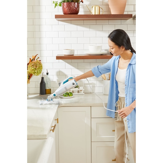 BLACKDECKER BHSM15FX08 steam cleaner in use on a kitchen countertop, white and blue handheld design.