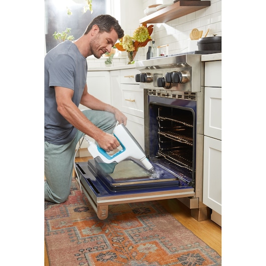 BLACKDECKER BHSM15FX08 steam cleaner cleaning oven door in kitchen setting, handheld model.