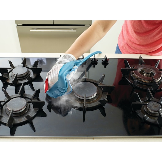 BLACKDECKER BHSM1615DAM steam cleaning glove cleaning a black gas stove top.