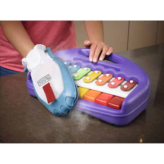 BLACKDECKER BHSM1615DSG steam glove cleaning a purple toy xylophone on a tabletop, close-up angle.