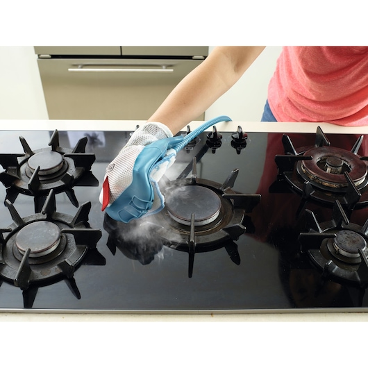 BLACKDECKER BHSM1615DSG steam cleaning glove used on a gas stove cooktop, photography front angle.