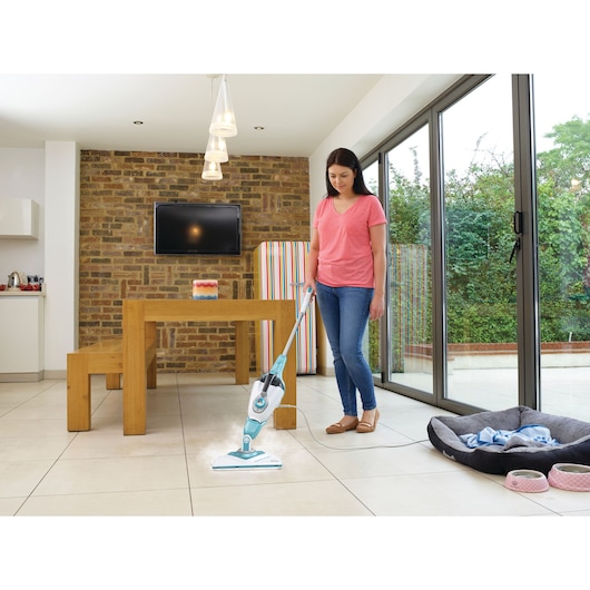 BLACKDECKER BHSM168U steam mop used on tile floor in a modern dining area with wood table and bench.