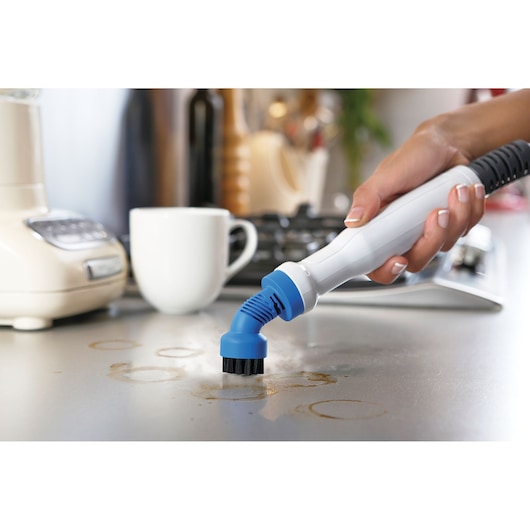 Photo of BLACKDECKER BHSM168U steam cleaner handheld brush cleaning a kitchen countertop with coffee stains.
