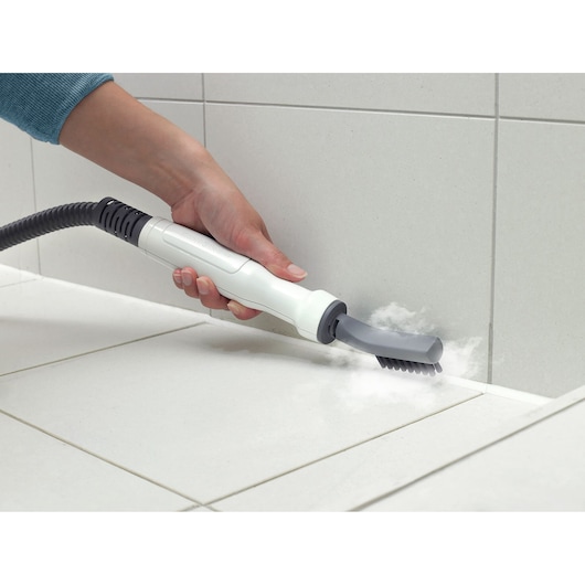BLACKDECKER BHSM169DSM steam cleaner nozzle with brush cleaning grout on white tiled floor, close-up.