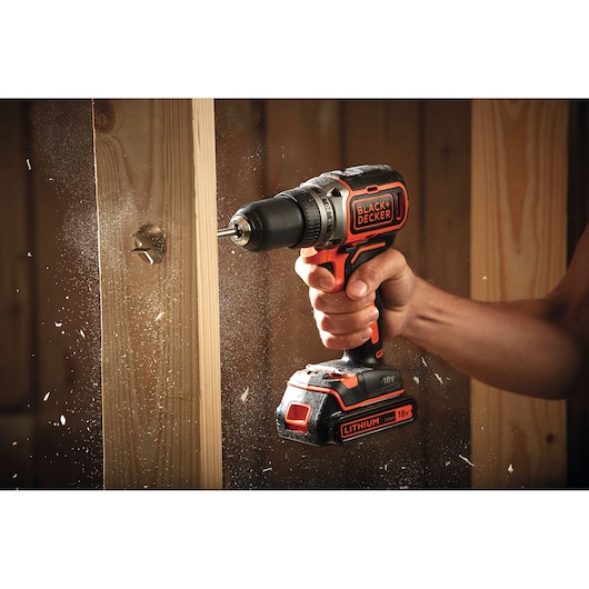 BLACK+DECKER BL186K1B2 cordless drill drilling into wood, close-up view with wood chips flying.