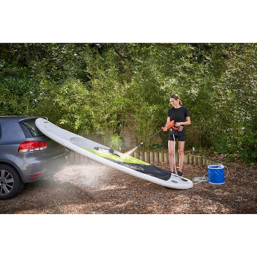BLACKDECKER BZOB1 portable pressure washer cleaning a paddleboard next to a car outdoors.