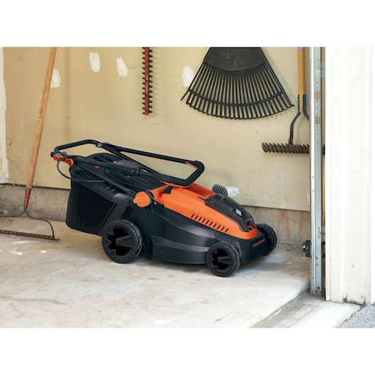 BLACKDECKER CLM3820L1 lawn mower with folded handle, orange and black, in a garage, side angle.