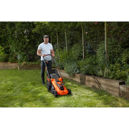 BLACKDECKER CLMA4820L2 orange cordless lawn mower on grass beside raised garden beds, outdoor use.