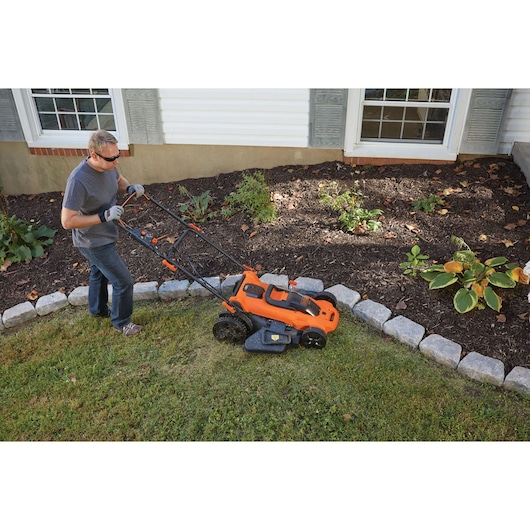 BLACKDECKER CLMA4820L2 orange cordless lawn mower in use near garden bed, side angle outdoors.