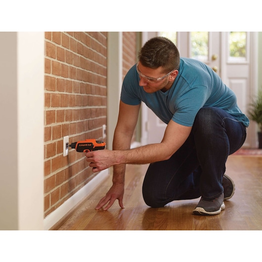Photo of person using BLACKDECKER CS36BST cordless screwdriver to install an outlet cover on a brick wall.