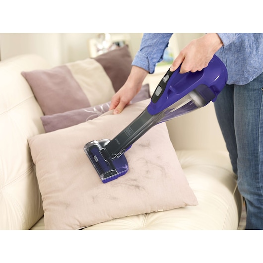 BLACKDECKER DVA325JP07 handheld vacuum cleaning pet hair from a beige pillow on a sofa.