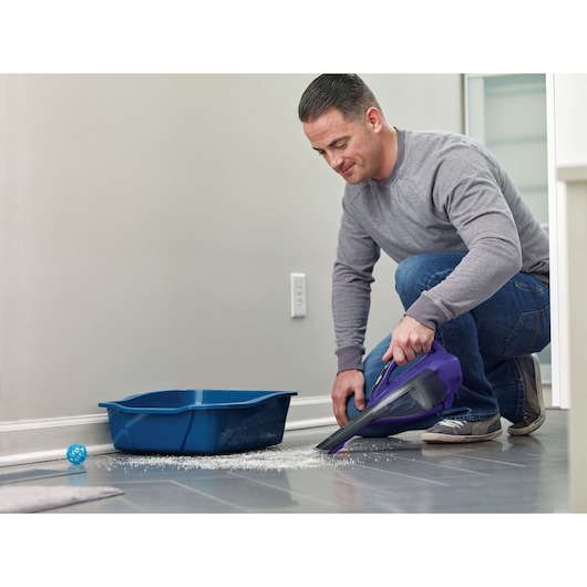 BLACKDECKER DVA325JP07 handheld vacuum cleaning spilled litter next to a blue tray on tile floor.