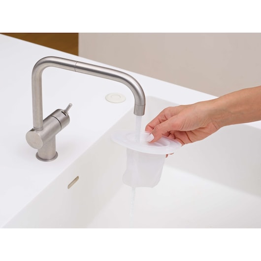 Photo of a hand rinsing BLACKDECKER DVJ315B vacuum filter under a kitchen faucet over a white sink.