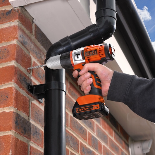 BLACKDECKER EGBHP1881BK cordless drill in use drilling into exterior brick wall near black piping.