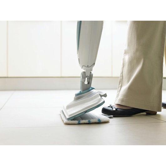 BLACKDECKER FSM1630 steam mop cleaning tile floor, close-up side view showing mop head and user’s foot.