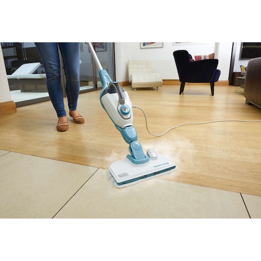 Photo of BLACK+DECKER FSMH1321JSM steam mop cleaning light wooden and tile floor in a modern living room.