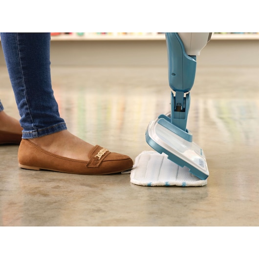 BLACK+DECKER FSMH1321JSM steam mop close-up on floor, person attaching cleaning pad with foot.